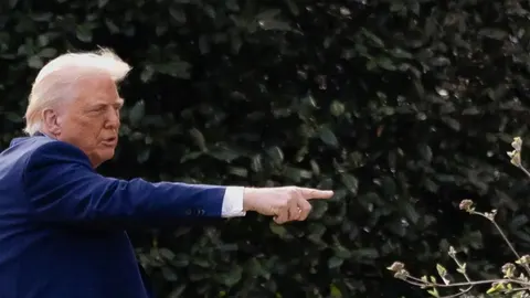 Donald Trump u plavom odelu pokazuje prstom u pravcu