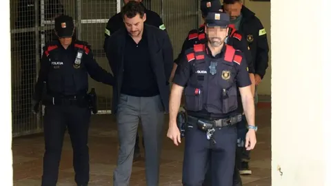 Muškarac u tamnom saku i sivi hlačama u pratnji policijaca