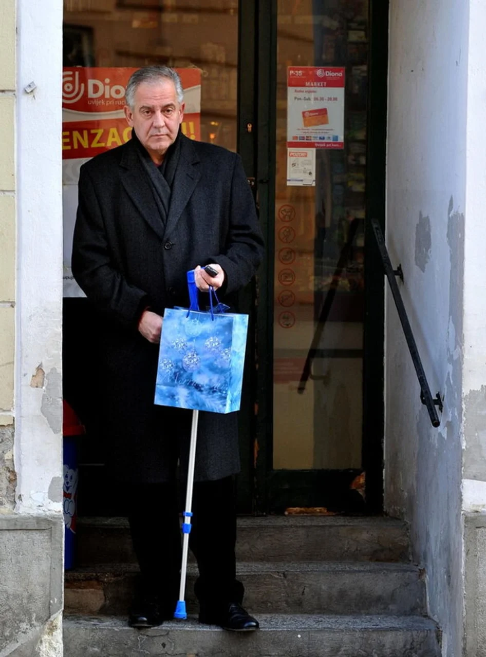 Muškarac u crnom kaputu koji se oslanja na štap