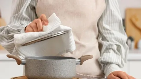 Osoba u kuhinji koristi krpu za podizanje poklopca s lonca