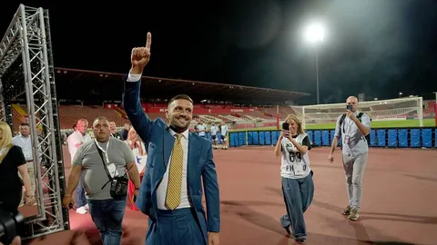 Dušan Tadić u plavom odielu s podignutim prstom na nogometnom stadionu