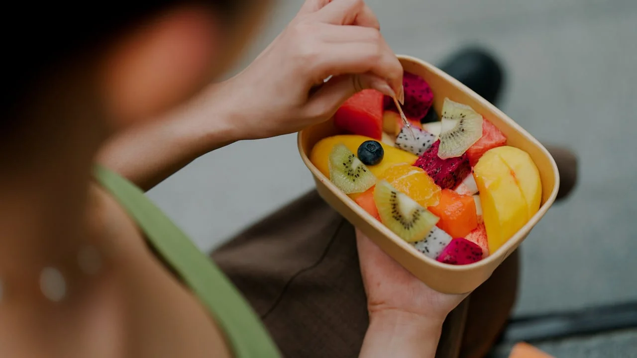 Žena koja jede šaliku mješanog voća s kivi, mango i pitajom