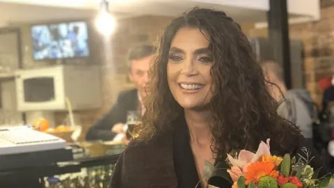Portret nasmijane pjevačice s kovrčavom kosom koja drži buket cvijeća