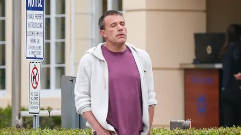 Ben Affleck u sivoj duksi i ljubičastoj majici stoji na otvorenom