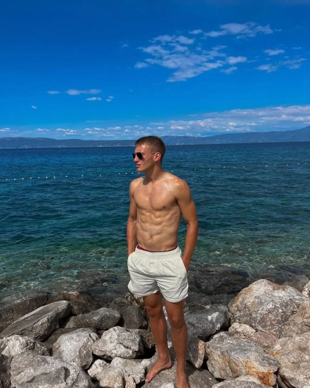 Muškarac bez majice u bijelim hlačama na kamenitoj obali