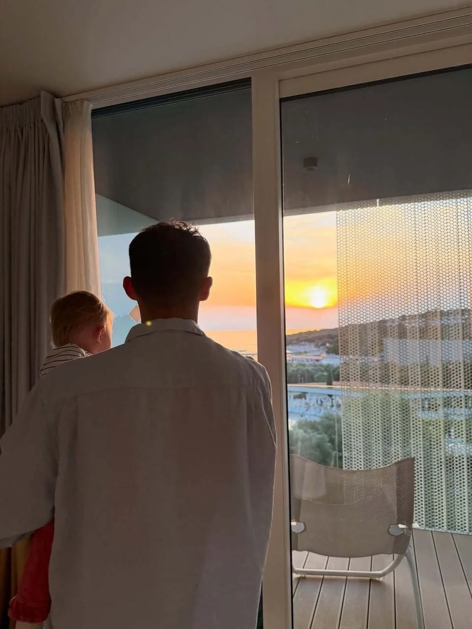 Muškarac s djetetom gledaju zalazak sunca kroz staklena vrata