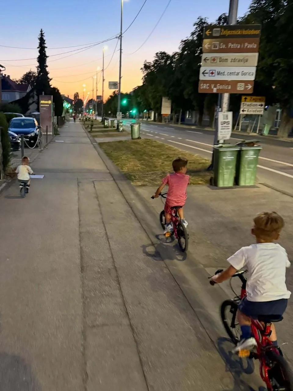 Troje djece vozi bicikle po pločniku u sumrak
