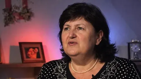 Portret žene srednjih godina u crnoj košulji na točkice s biserima