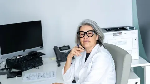 Srednje godine žena u bijelom liječničkom mantilu i crnim naočalama u uredu