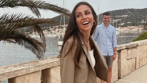 Nasmijana žena i muškarac pored kamene ograde uz obalu s jahtama