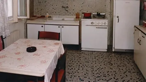 Kuhinja s retro pločicama s sitnim uzorkom, bijelim uređajima i stolom s cvjetnim stolnjakom