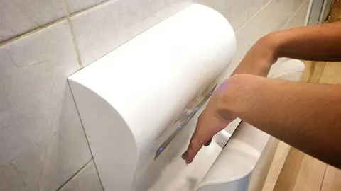 Ruke osobe koje se suše u bijeloj automatskoj sušilici ruku