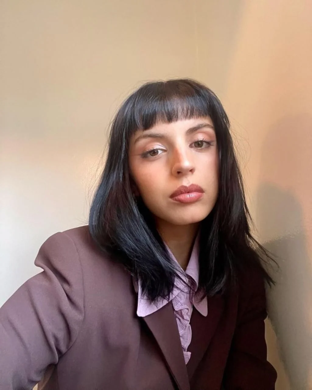 Žena s ravnom crnom kosom i šiškama u ljubičastom saku