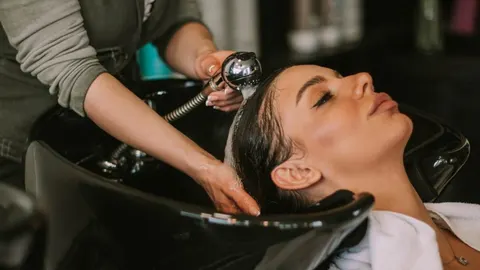 Frizerka pere tamnu kosu klijentice u crnom salonu