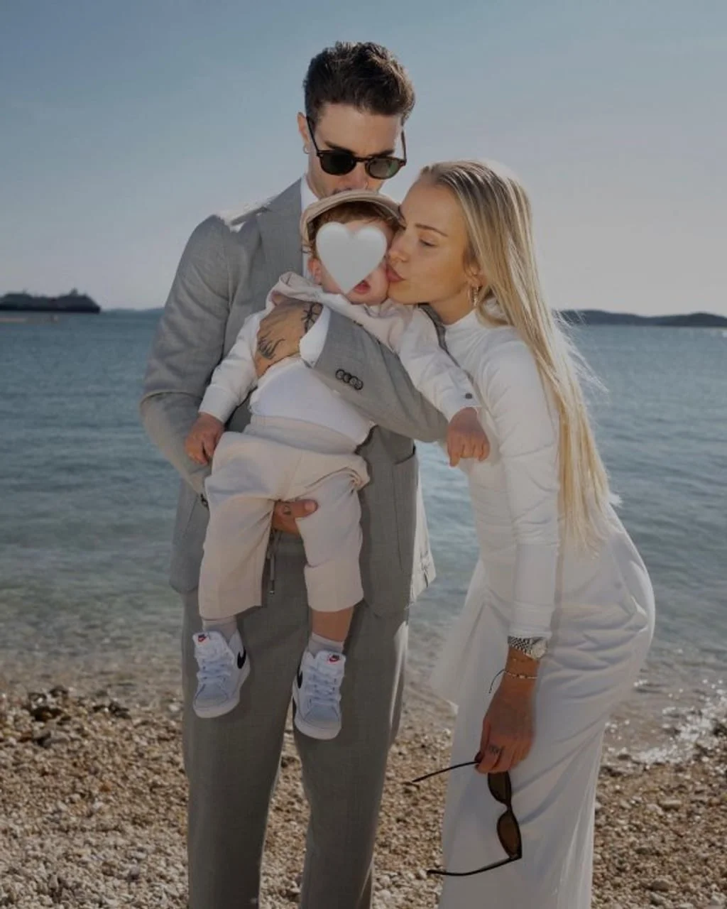 Obitelj na plaži, muškarac drži dijete dok ga žena ljubi u obraz