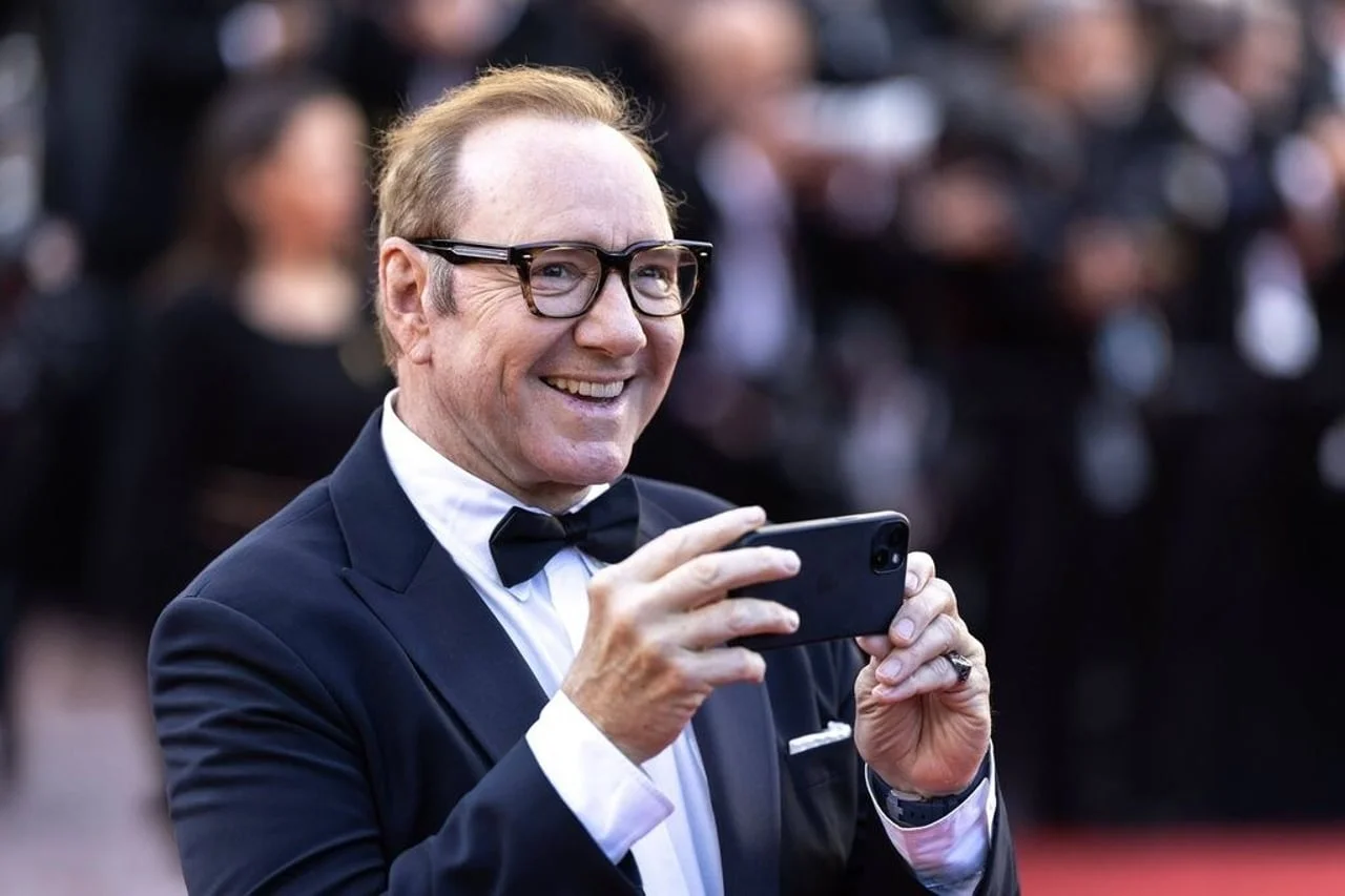 Kevin Spacey u smockingu koji drži pametni telefon u rukama