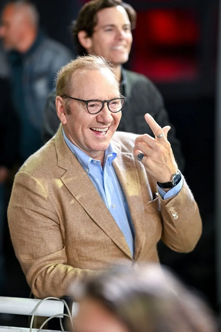 Kevin Spacey u bež saku i plavoj košulji, nasmijan i gestikulira