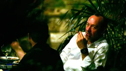 Kevin Spacey u bijeloj košulji puši cigaretu u večernjem ambijentu