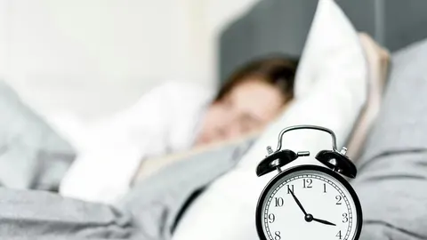 Crni alarmni sat u prvom planu, osoba koja spava u pozadini