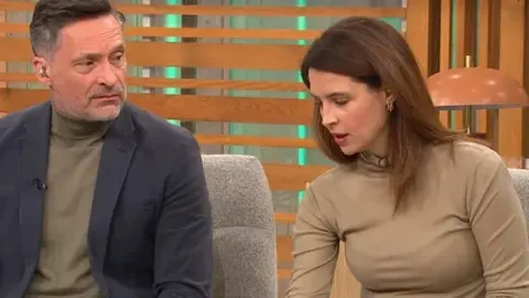 Voditelji u televizijskom studiju gledaju prema dolje s izrazom zabrinutosti.