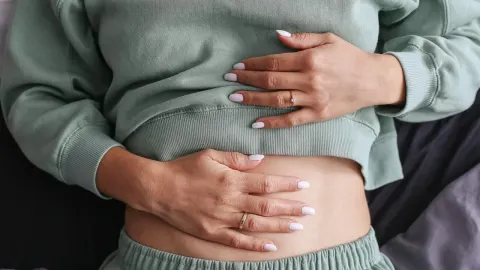 Žena drži dlanove na trbuhu preko pamučne majice