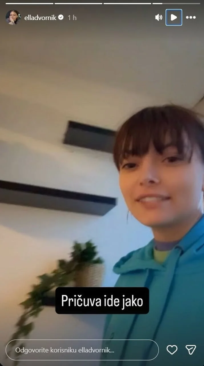 Influencerica stoji u zatvorenom prostoru ispred polica na zidu