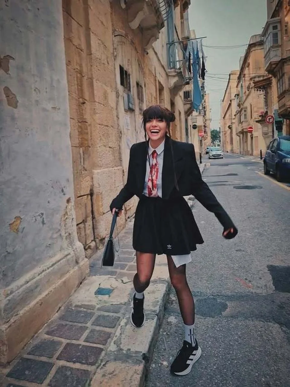 Ella Dvornik u crnom kostimu s torbicom nasmijana hoda ulicom