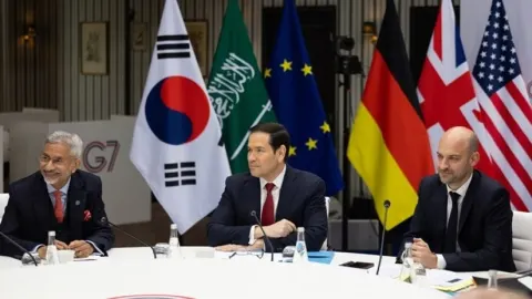 Marco Rubio sjedi za okruglim stolom ispred zastava na sastanku skupine G7.