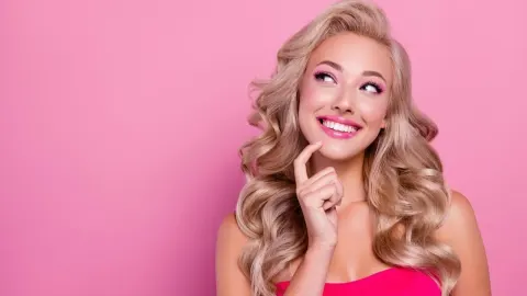 Nasmijana plavuša gleda u stranu i razmišlja na ružičastoj pozadini