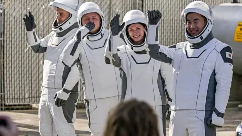 Četiri astronauta u bijelim svemirskim odijelima mašu i pozdravljaju.