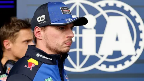 Max Verstappen u timskoj odjeći s kapom i ozbiljnim izrazom lica ispred FIA logotipa.