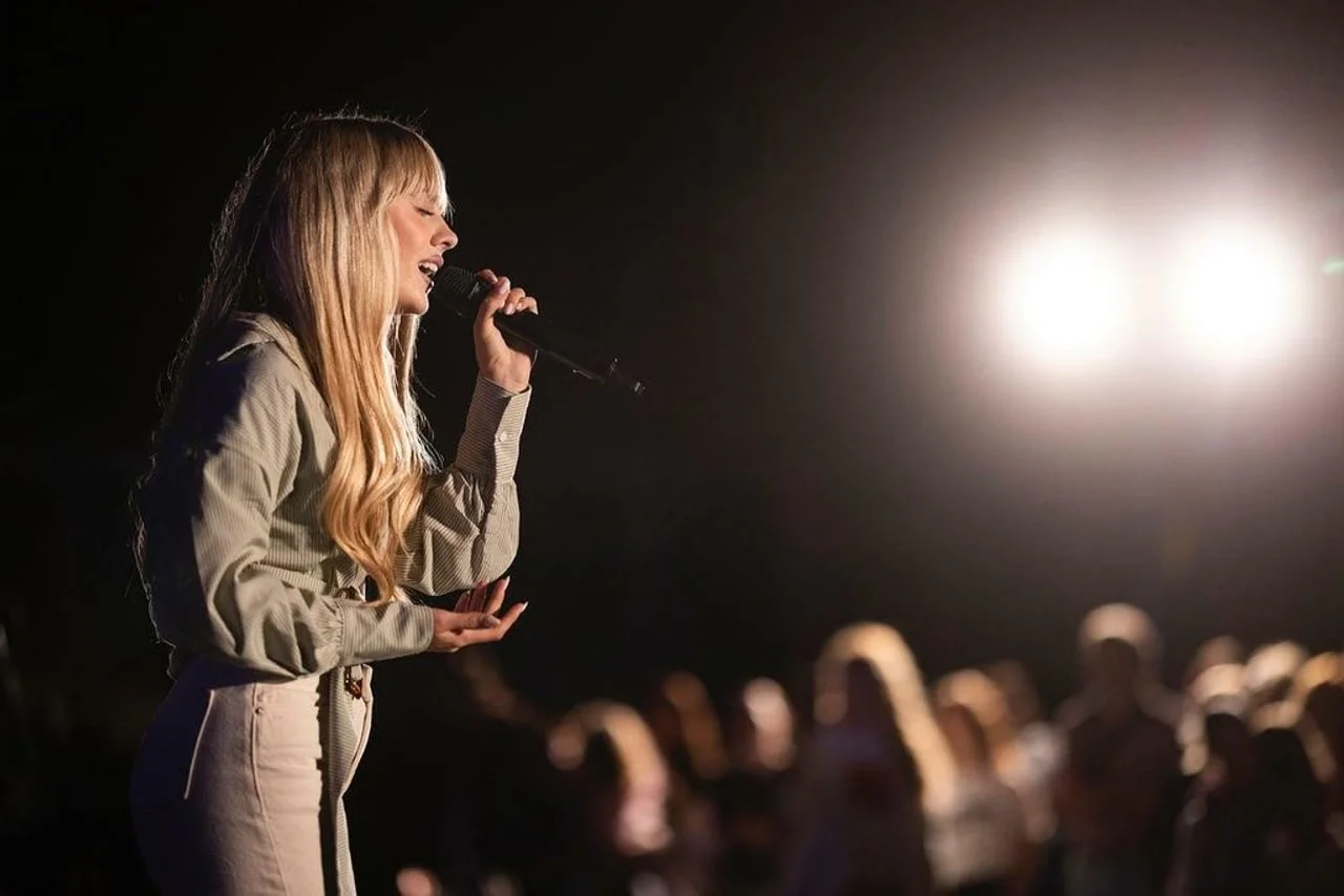 Albina pjeva na pozornici s mikrofonom pod reflektorima