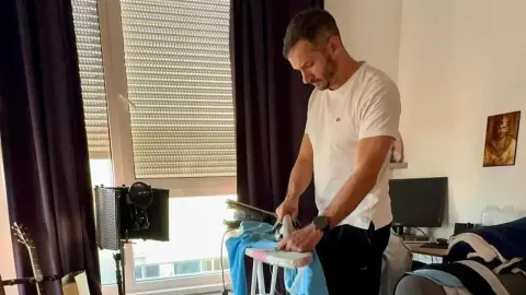 Glazbenik Boris Rogoznica u bijeloj majici pegla odjeću u svojem domu.