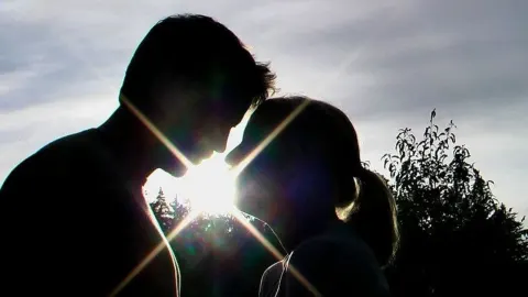 Silueta muškarca i žene okrenutih licem prema licu uz jarku sunčevu svjetlost.