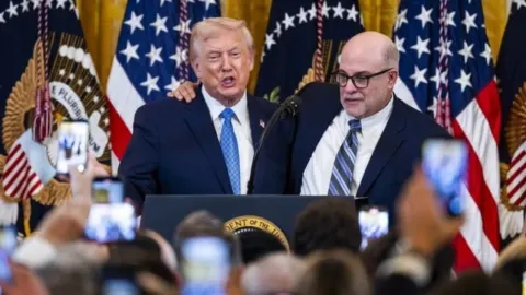 Donald Trump i Mark Levin govore na podiju ispred američkih zastava.