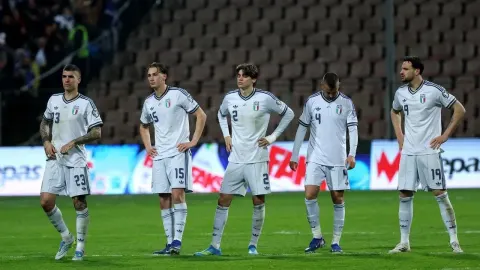 Talijanski nogometaši u bijelim dresovima stoje razočarani na travnjaku.