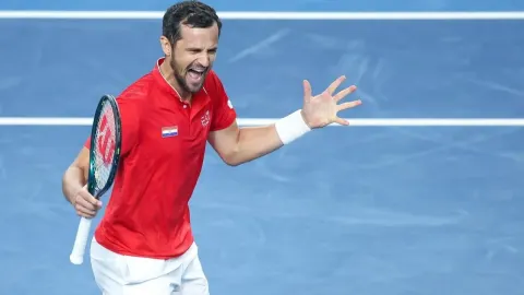 Hrvatski tenisač u crvenoj majici slavi bod na teniskom terenu s reketom u ruci.