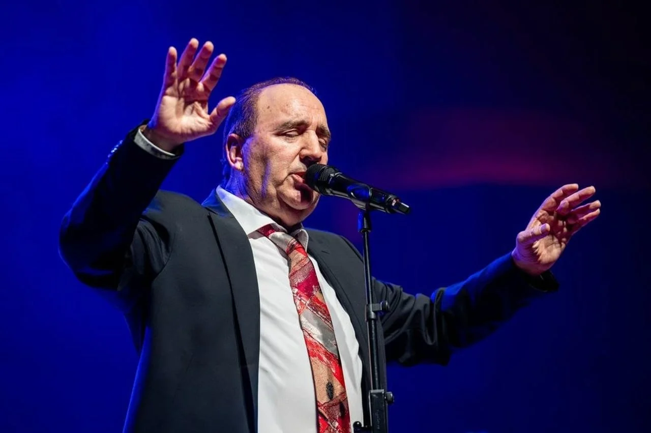 Pjevač na pozornici s podignutim rukama ispred mikrofona