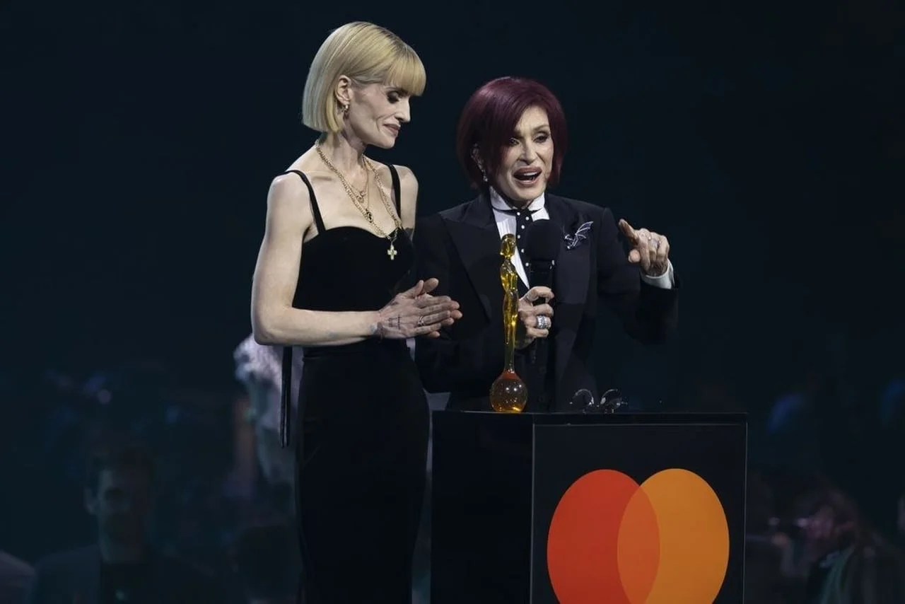 Široki kadar Kelly i Sharon Osbourne za govornicom s kipićem