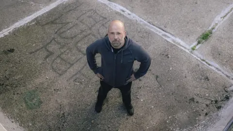 Sredovječni muškarac s bradom gleda prema gore dok stoji na betonskom platnu.