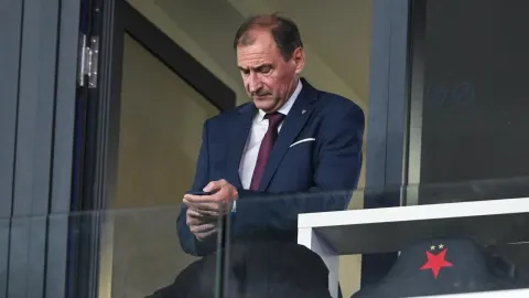 Božidar Šikić u tamnom odijelu gleda u svoj mobilni telefon na stadionu.