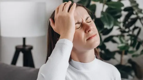 Mlada žena s bolnim izrazom lica drži ruku na čelu zbog jake glavobolje.