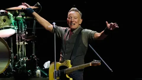 Bruce Springsteen s gitarom na pozornici s podignutim rukama