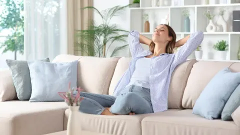 Žena sjedi na kauču s rukama iza glave u dnevnom boravku.