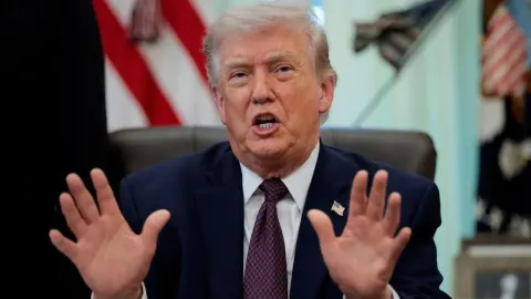 Donald Trump govori s podignutim rukama ispred američke zastave u zatvorenom prostoru.