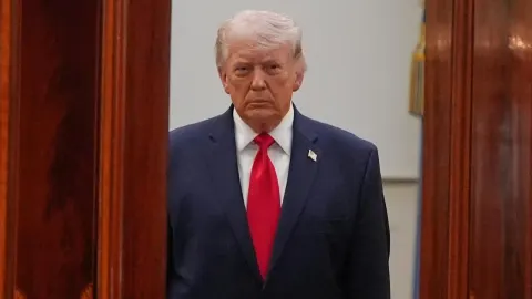 Donald Trump u tamnom odijelu s crvenom kravatom gleda prema kameri.