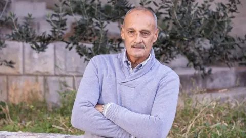 Marin Kurtela u plavom džemperu pozira prekriženih ruku ispred kamenog zida.