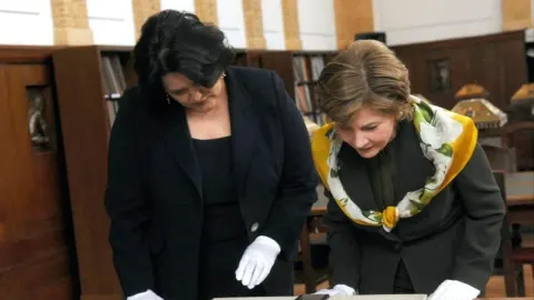 Sredovječna žena s crnom kosom i žena s maramom gledaju u predmet.