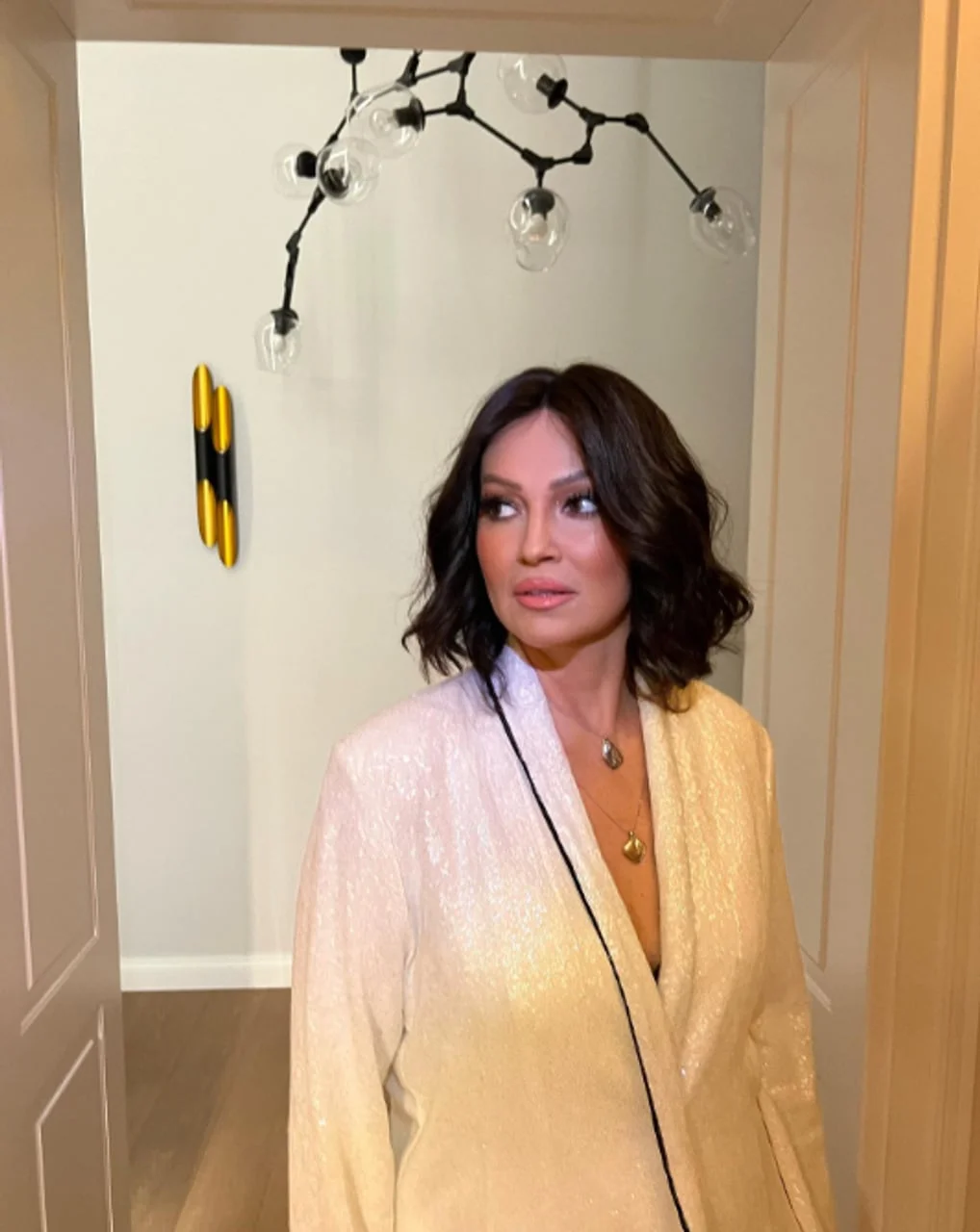 Nina Badrić u bijelom sakuu s modernim lusterom u pozadini