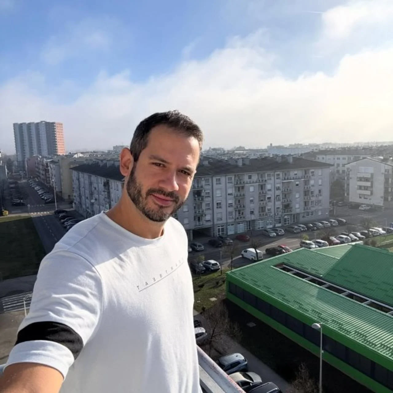 Boris Rogoznica u bijeloj majici pozira na balkonu s pogledom na gradske zgrade.